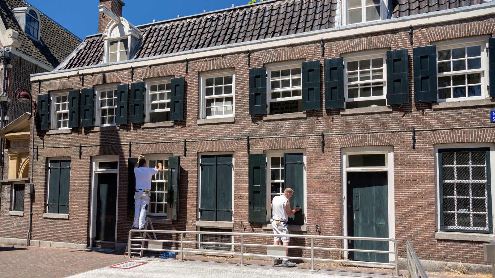 Two painters refurbishing the traditional Dutch brick house facade on a sunny day