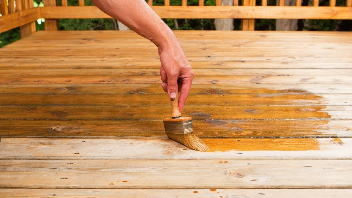 applying a dark brown wood stain to a wooden deck